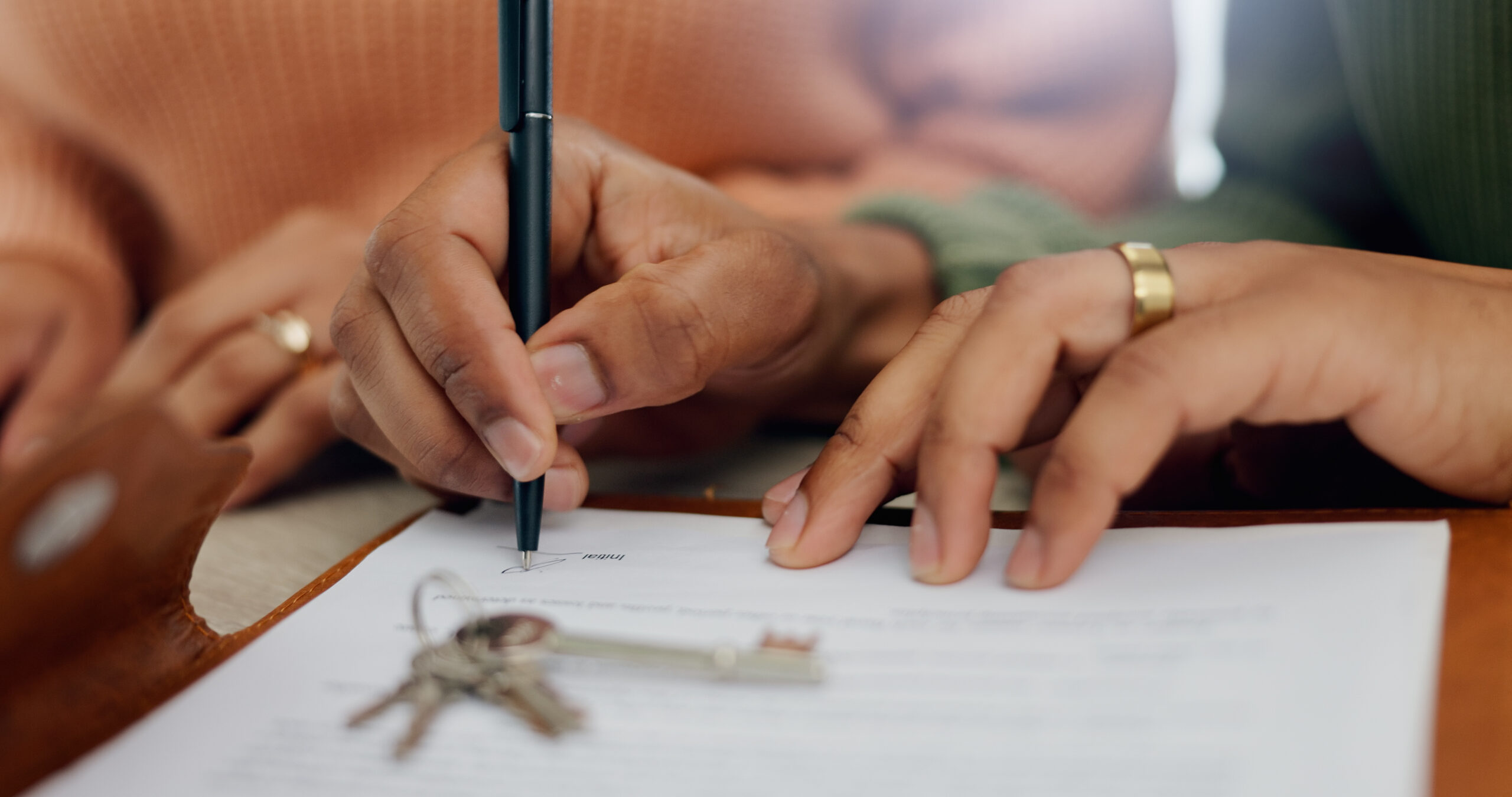 Closeup, hands and signature on mortgage paperwork for finance, home contract or a loan. Investment, legal and a couple writing on a document for keys of a house, ownership and agreement for a deal.