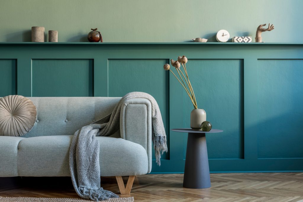 Creative interior design of living room at cozy apartment with stylish sofa, plants, design furnitures, decoration and elegant accessories. Green walls, parquet floor. Home staging. Template.